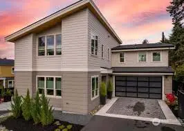 Front elevation of a modern tan house with new windows and a dark garage door at dusk