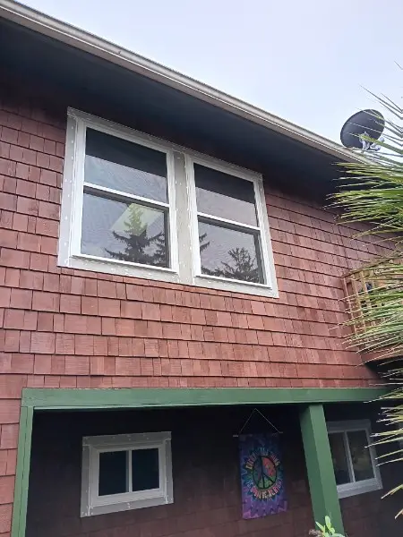Two upper-story windows on a redwood shake house above a green porch beam
